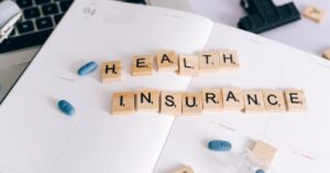 Scrabble tiles spelling 'Health Insurance' on planner with pills and laptop, symbolizing healthcare planning/Studentische Krankenversicherung Deutschland
