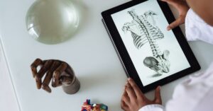 Hands examining a digital anatomy illustration on a tablet alongside anatomical models on a table.